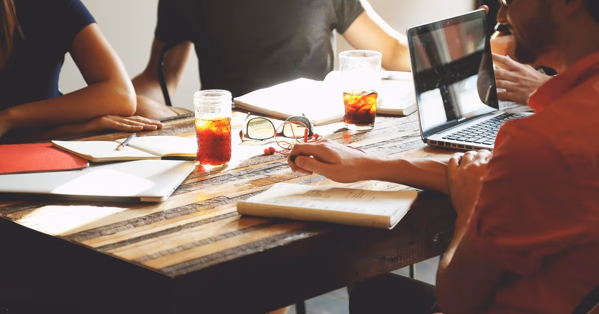 Three teammates sharing one customer inbox on a laptop and a phone at a small office table, representing Front app alternatives in 2026