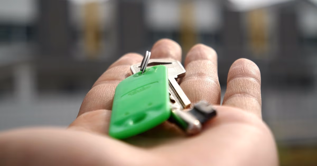 Agente inmobiliario gestionando consultas de compradores y vendedores desde WhatsApp en el móvil frente a una propiedad