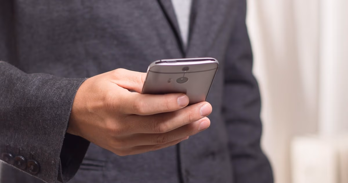 Business owner in a suit holding a smartphone, representing getting a verified business account on WhatsApp